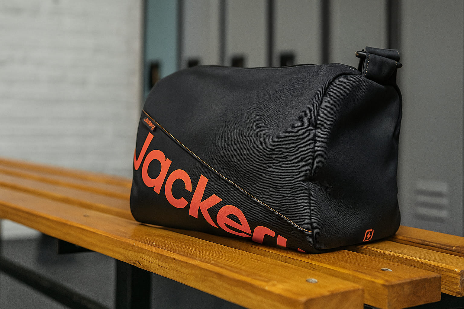 Black bag with red text on a wooden bench in front of lockers