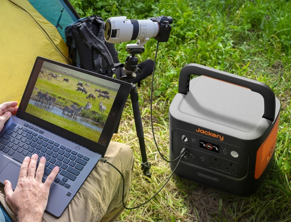 A man sat on the grass, operating his laptop, which was connected to an external camera. The screen showed him filming zebras. A Jackery 2000v2 was powering both devices.